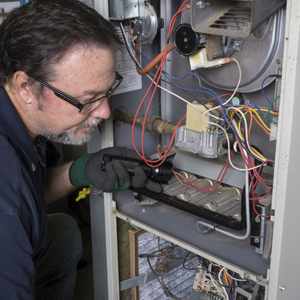 Techician looking over a gas furnace with a flashlight before cleaning it.